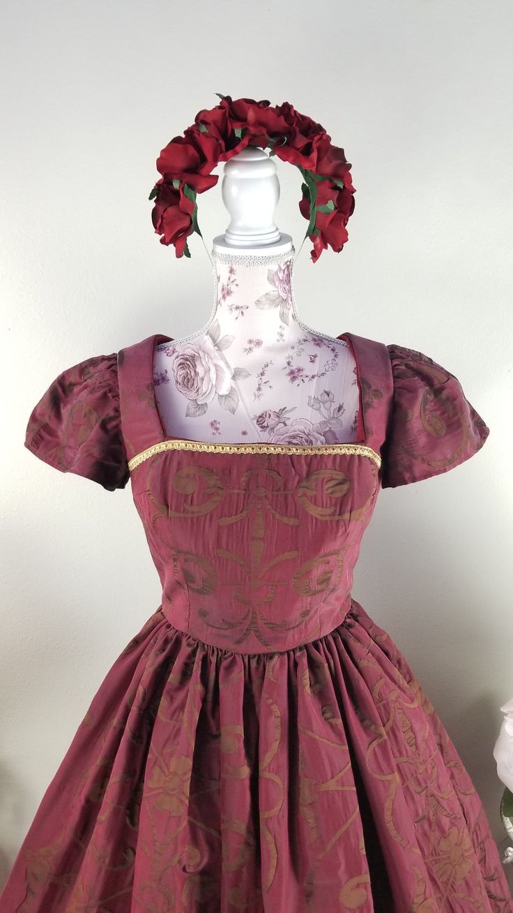 This rich in burgundy color is designed as a one-of-a-kind dress by PMdesigns by Pamela Marie. It has a gorgeous embroidery pattern throughout, and a gold trim around the hem of a full skirt with hidden pockets, and matching trim on the front bodice. The back is cut in a V, and has a zipper up the back. Suggested measurements: 34" Bust x 26" Waist x Hips Free Fitted Red Dress With Historical Design, Red Formal Dress With Historical Design, Traditional Fitted Dress With Historical Design, Fitted Brocade Ball Gown Dresses, Red Fitted Brocade Dress, Fitted Brocade Ball Gown, Elegant Fitted Dress With Historical Design, Fitted Brocade Dress For Costume Party, Fitted Gold Dress For Costume