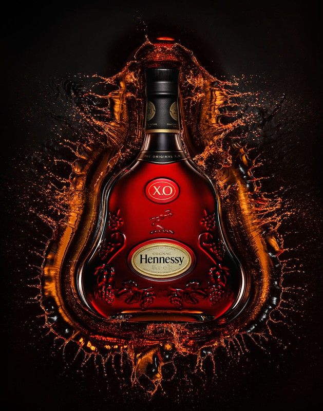 a bottle of hennesy xo on a black background with orange and yellow splashing around it