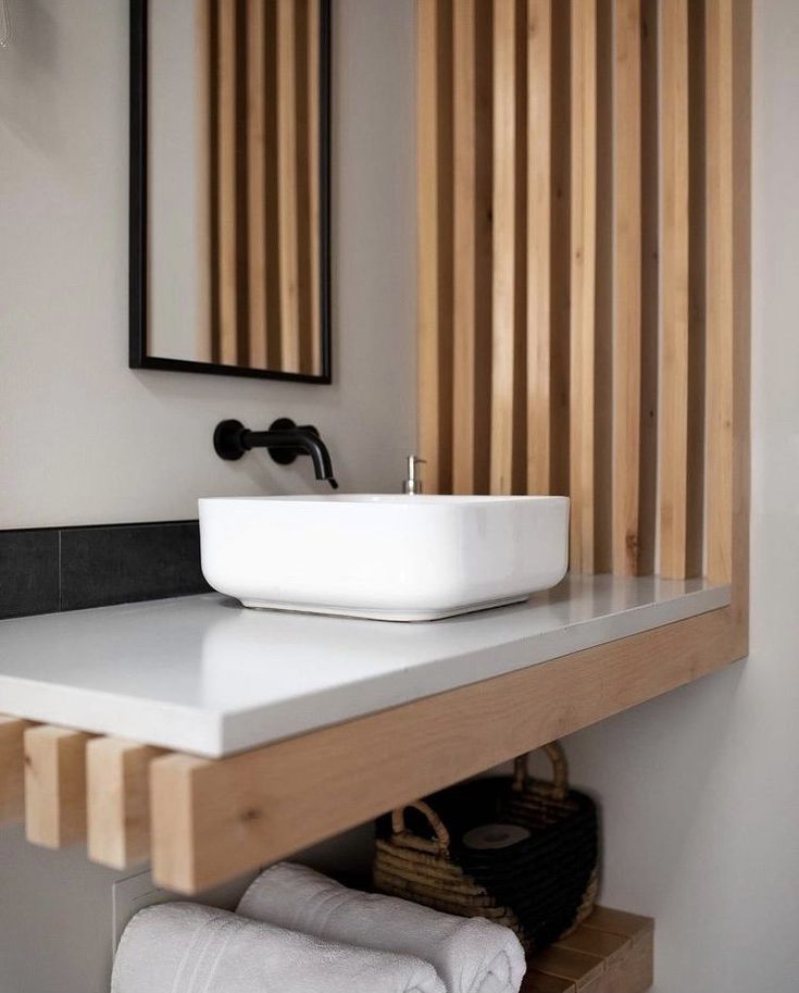 a white sink sitting under a mirror next to a wooden shelf with towels on it