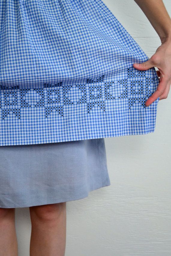 a woman wearing a blue and white checkered dress with her hands on the skirt