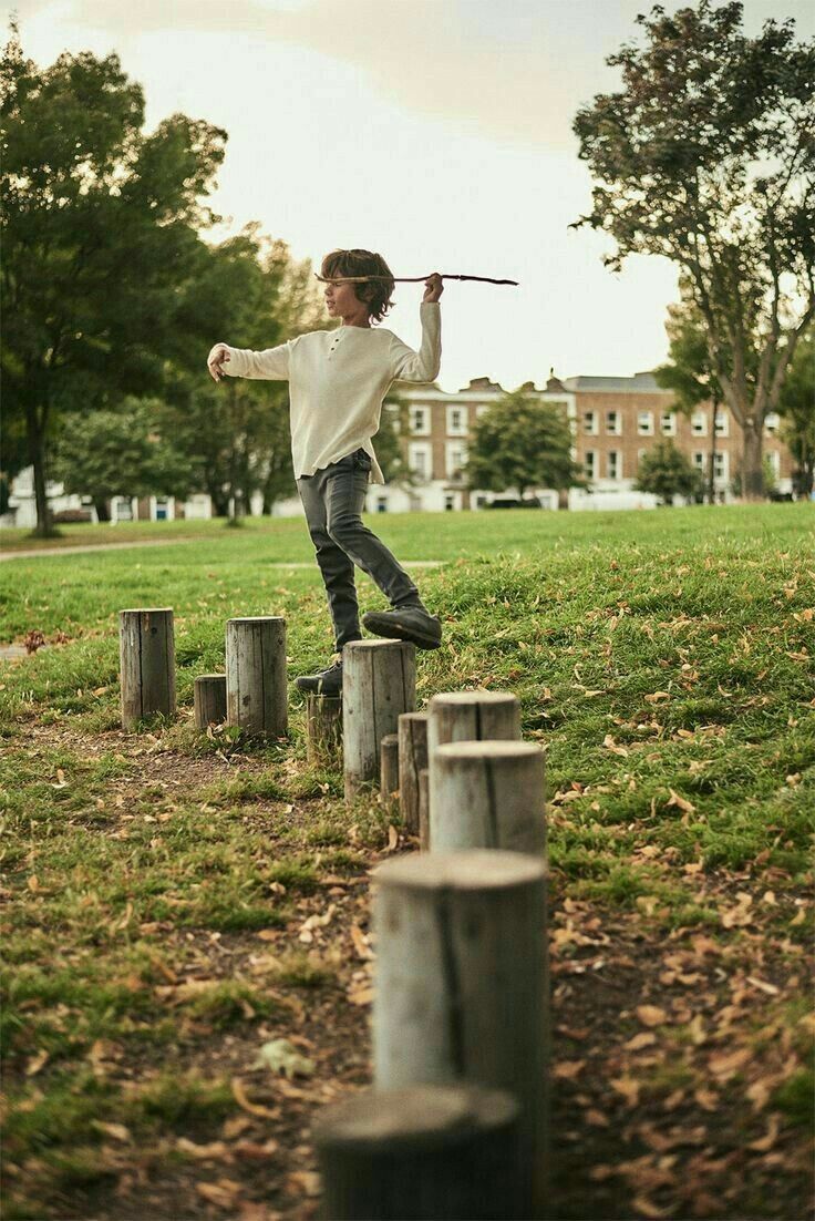 a young boy standing on top of wooden stumps holding a stick in his hand