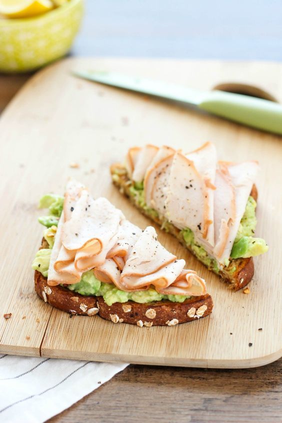 a sandwich with lettuce, cheese and other toppings sitting on a cutting board