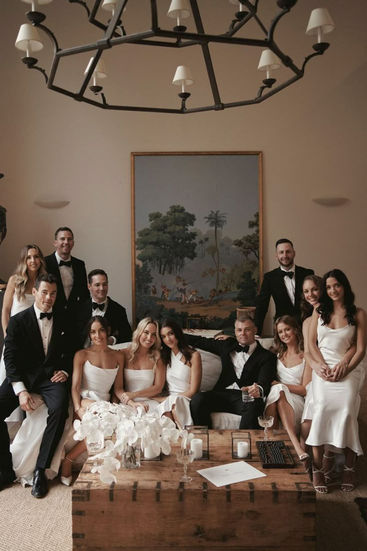 a large group of people in formal wear posing for a photo with one man on the couch