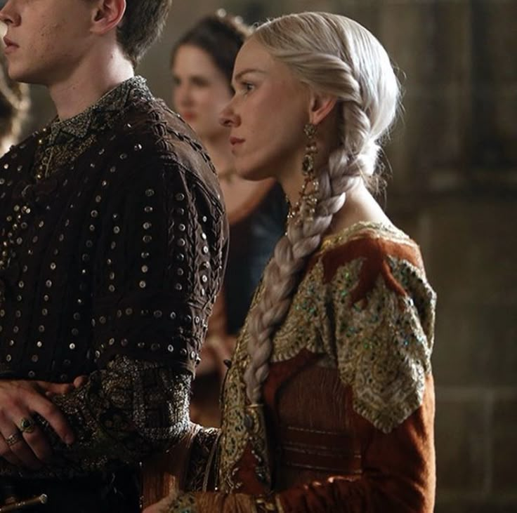 two people standing next to each other in medieval clothing and braids on their hair