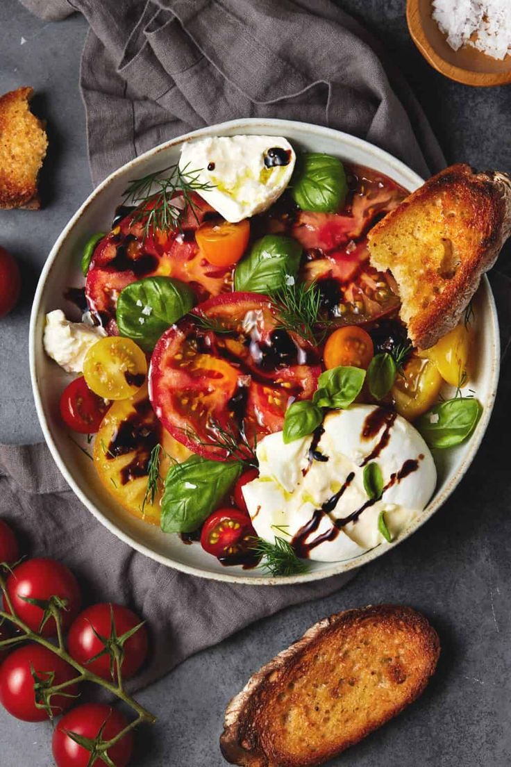 a white bowl filled with tomatoes, mozzarella cheese and bread on top of a table