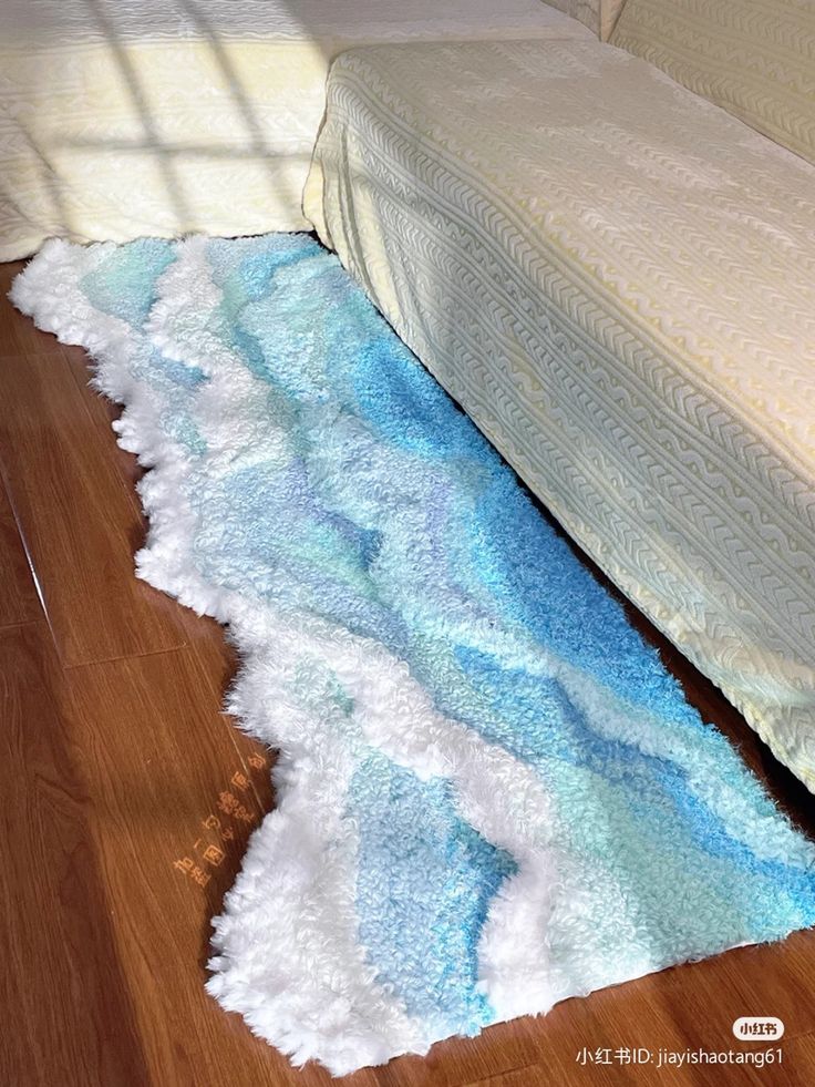 a bed sitting on top of a hard wood floor next to a rug covered in blue and white waves