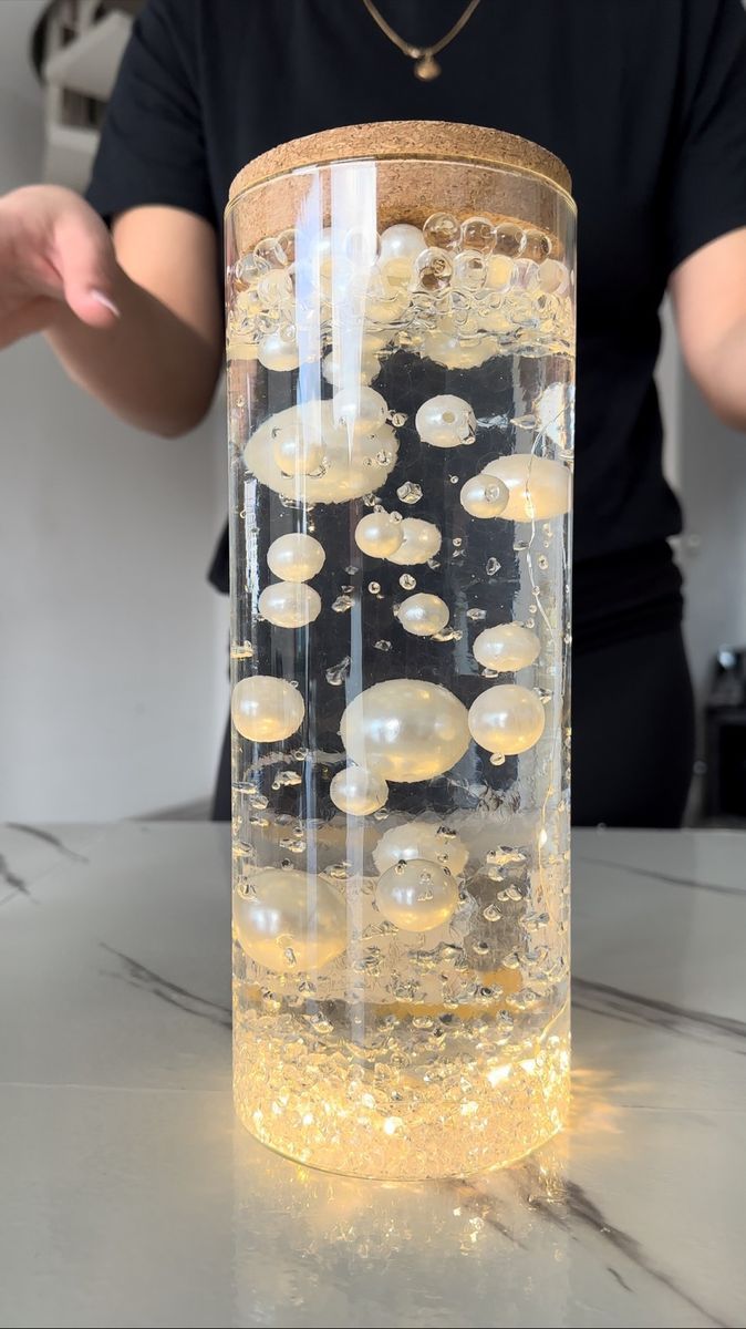 a glass filled with liquid sitting on top of a counter next to a person standing behind it