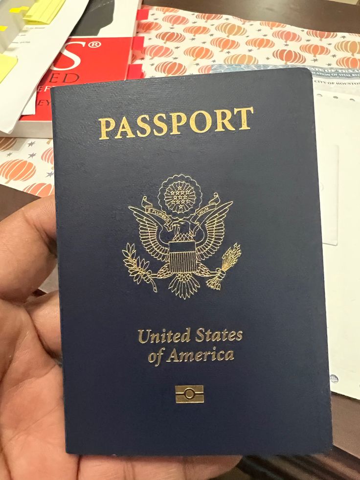 a person holding up a us passport in front of a pile of other papers and envelopes