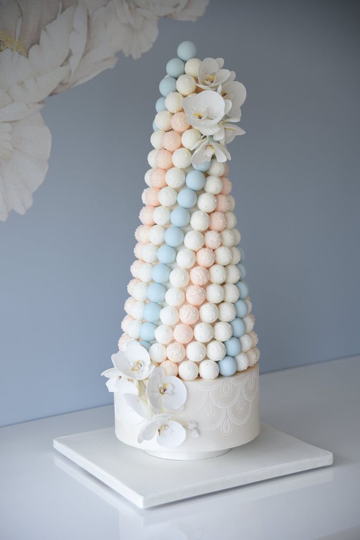 a cake decorated with pastel colors and flowers on a white tablecloth in front of a blue wall