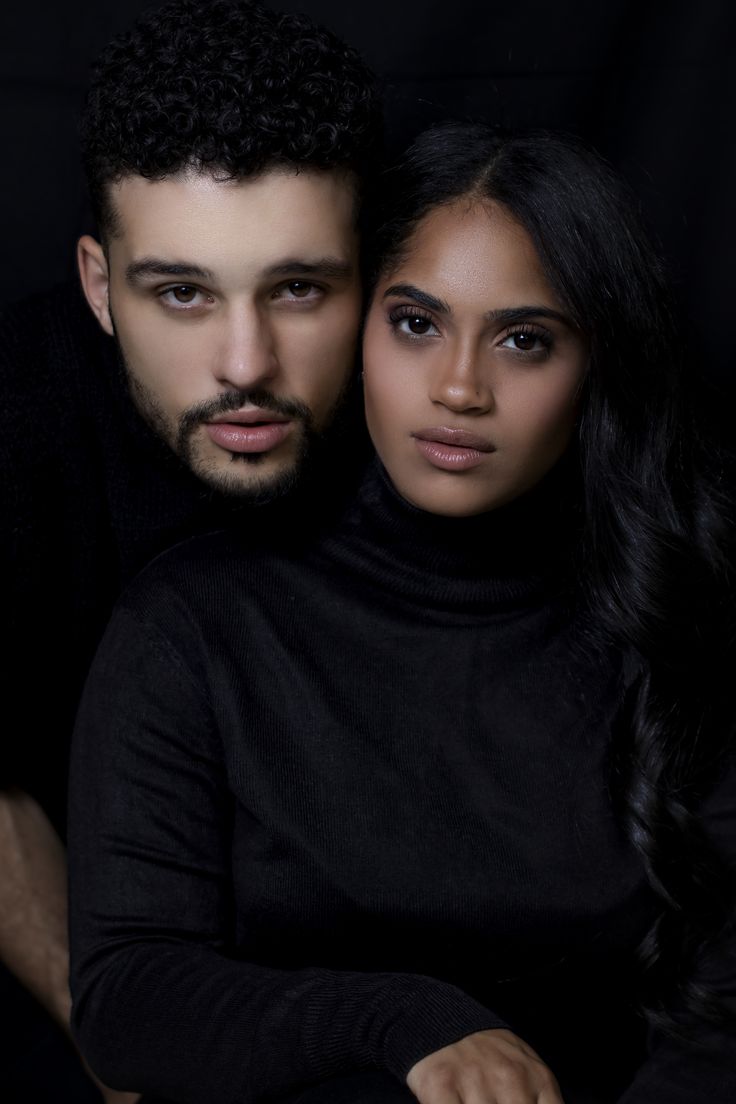 a man and woman sitting next to each other in front of a black background with their arms around each other