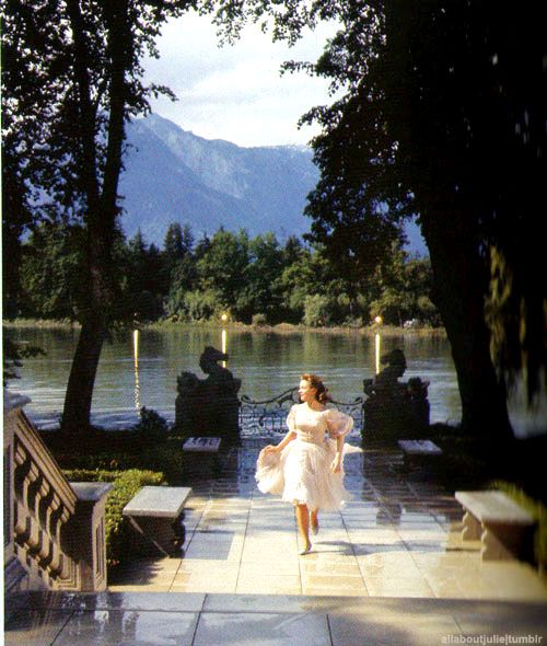 a woman in a white dress is walking down the sidewalk near some trees and water