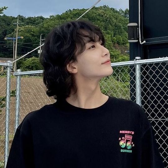 a young man standing in front of a fence with his eyes closed and looking up