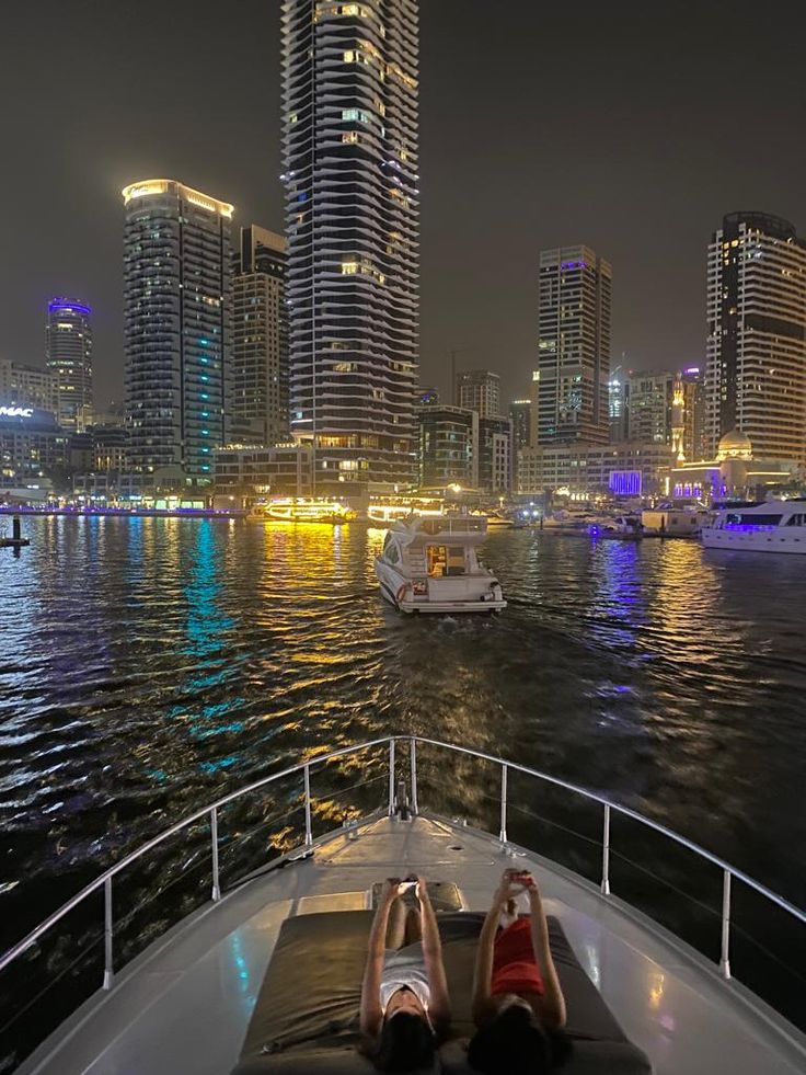 two women are lounging on the back of a boat in front of some tall buildings