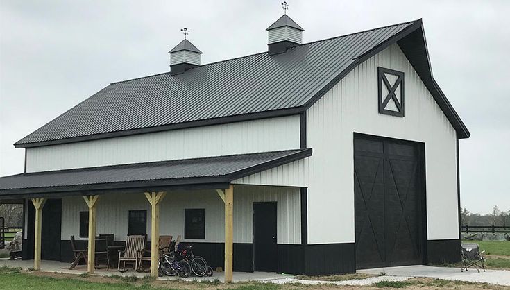 a large white barn with a black roof and two bicycles parked in the front yard