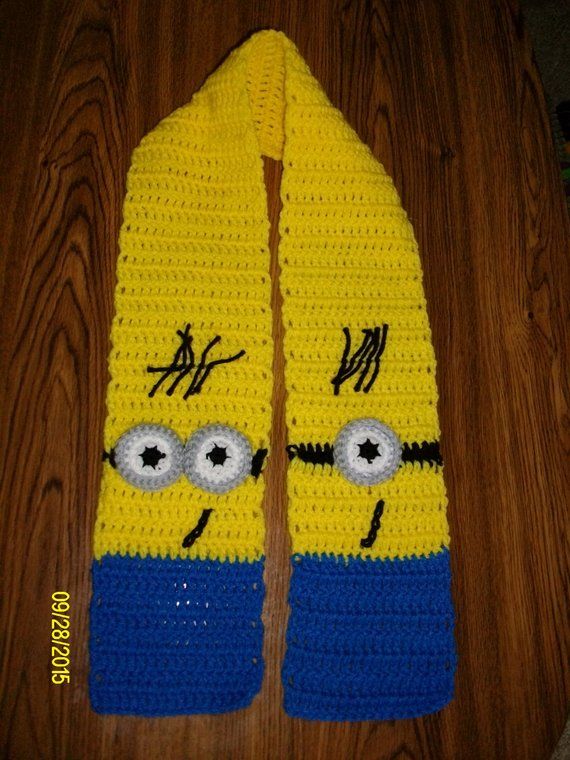 a crocheted yellow scarf with blue trim and eyes on it sitting on a wooden floor