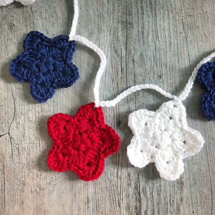 three crocheted flowers are hanging from strings on a wooden surface, one is red white and the other is blue