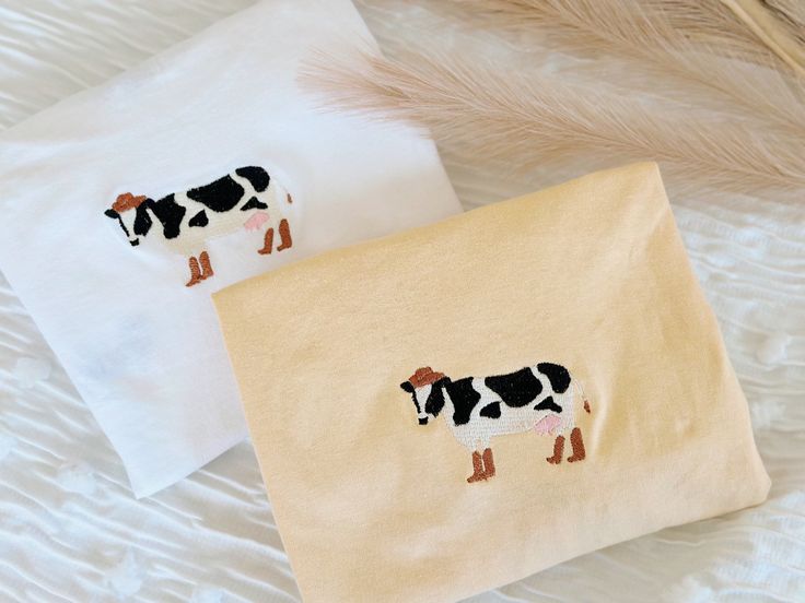 two towels with black and white cows on them sitting on a bed next to feathers