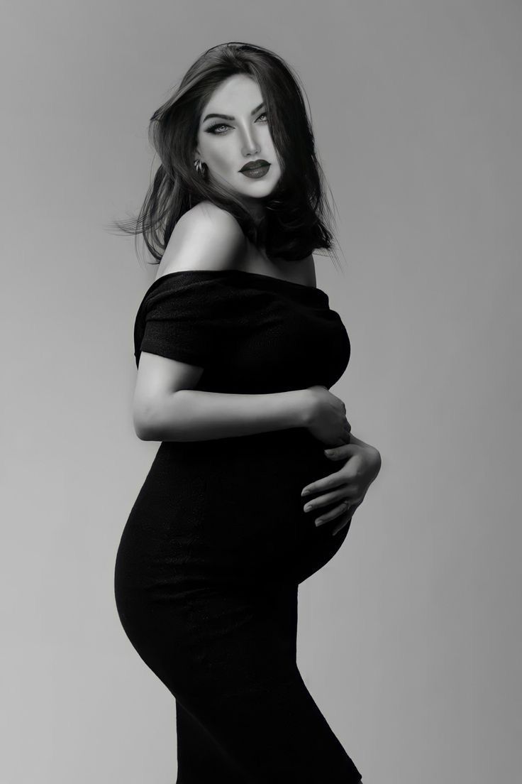 a pregnant woman poses for a black and white photo with her hands on her belly