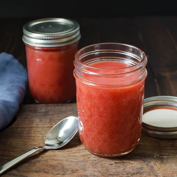 two jars filled with red sauce on top of a wooden table next to a spoon