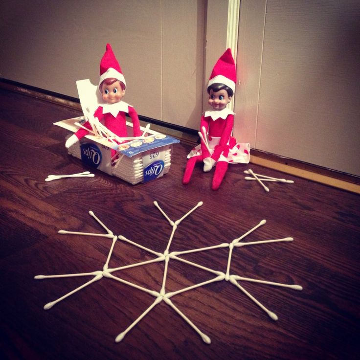 two elfs are sitting on the floor next to an open box with sticks sticking out of it