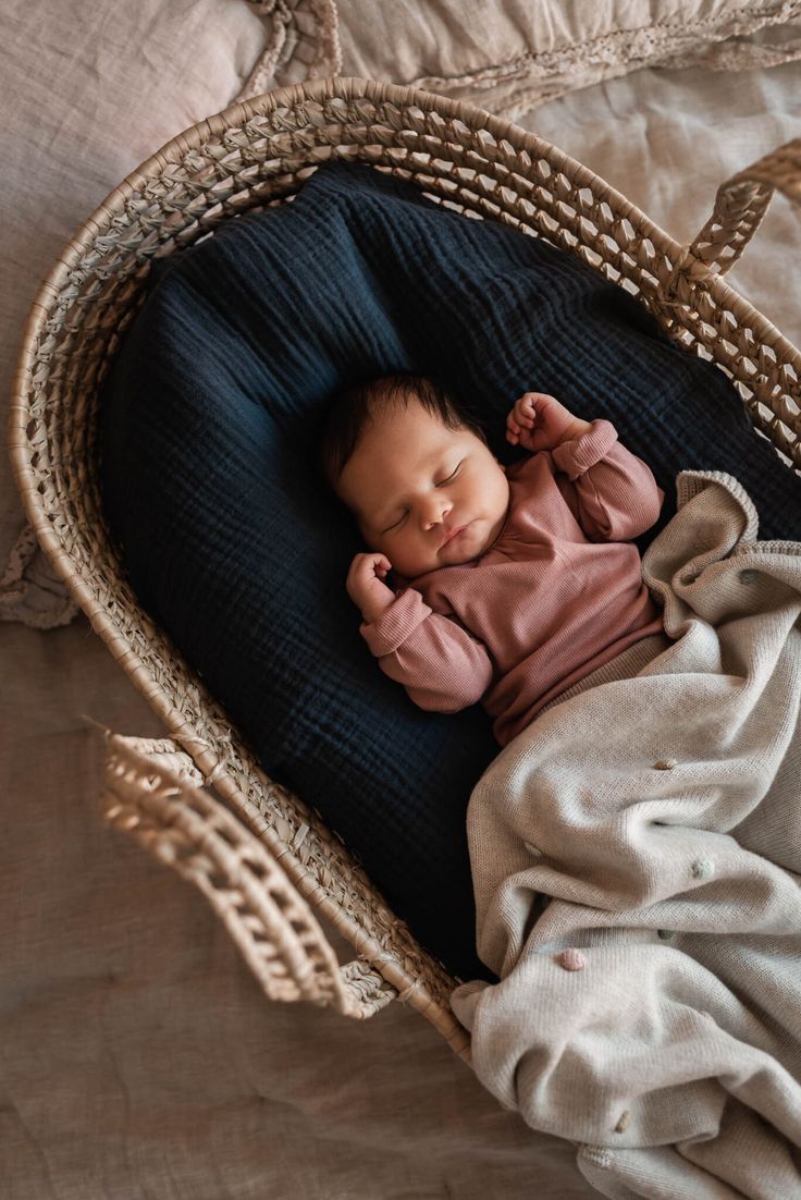 a baby sleeping in a basket on top of a bed