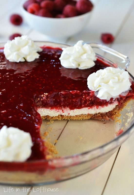 a pie with whipped cream and raspberries in the background