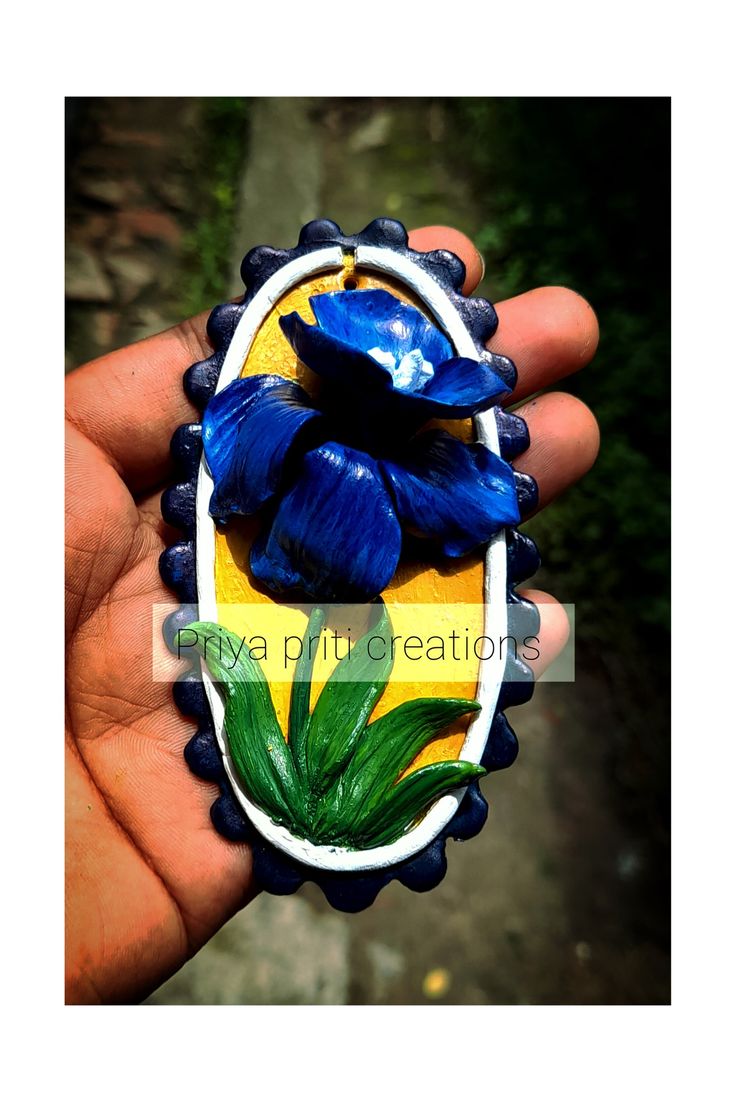 a hand holding a blue and yellow flower brooch