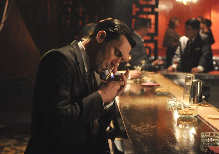 a man in a suit sitting at a bar with his cell phone to his ear