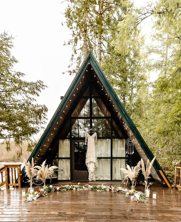 a wooden deck with a teepee tent and clothes hanging on the door, surrounded by greenery