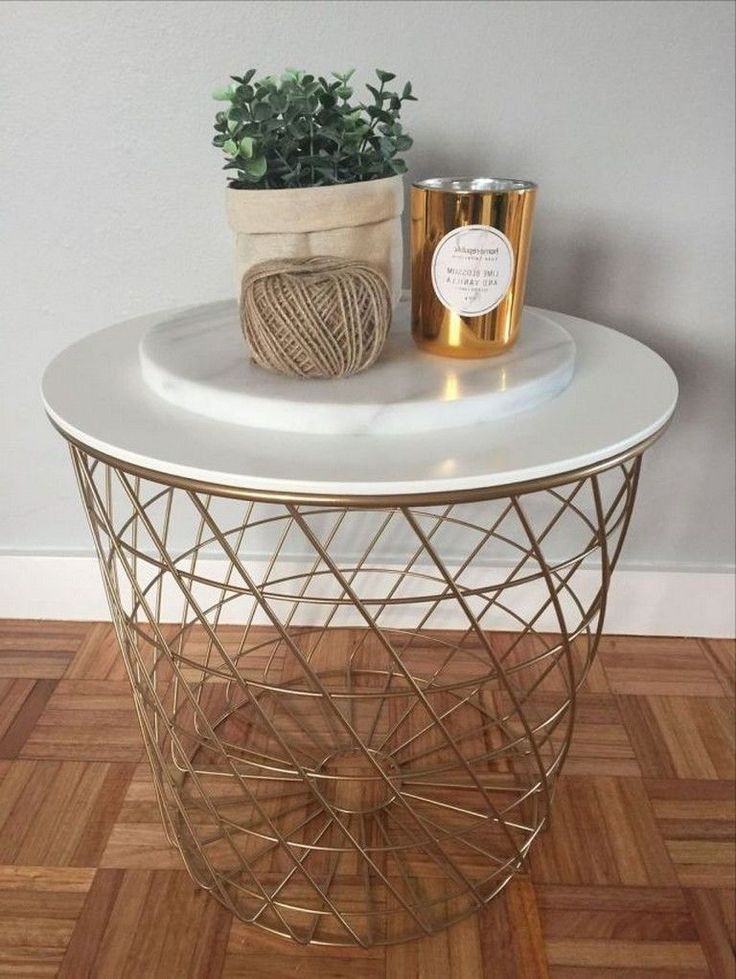 a white table topped with a potted plant next to a gold candle holder on top of a wooden floor