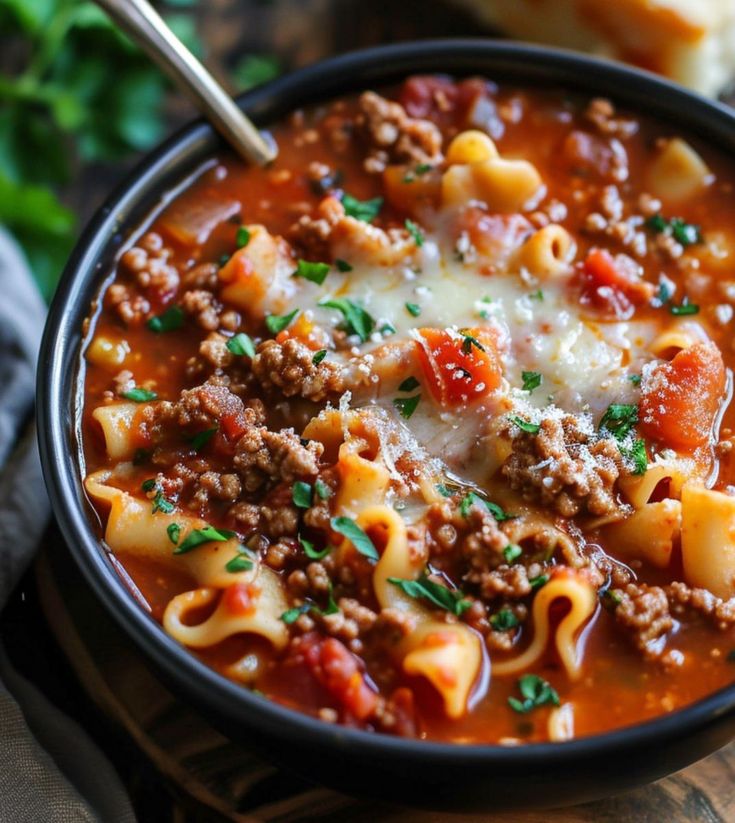 a bowl of pasta soup with meat and cheese on the side, ready to be eaten