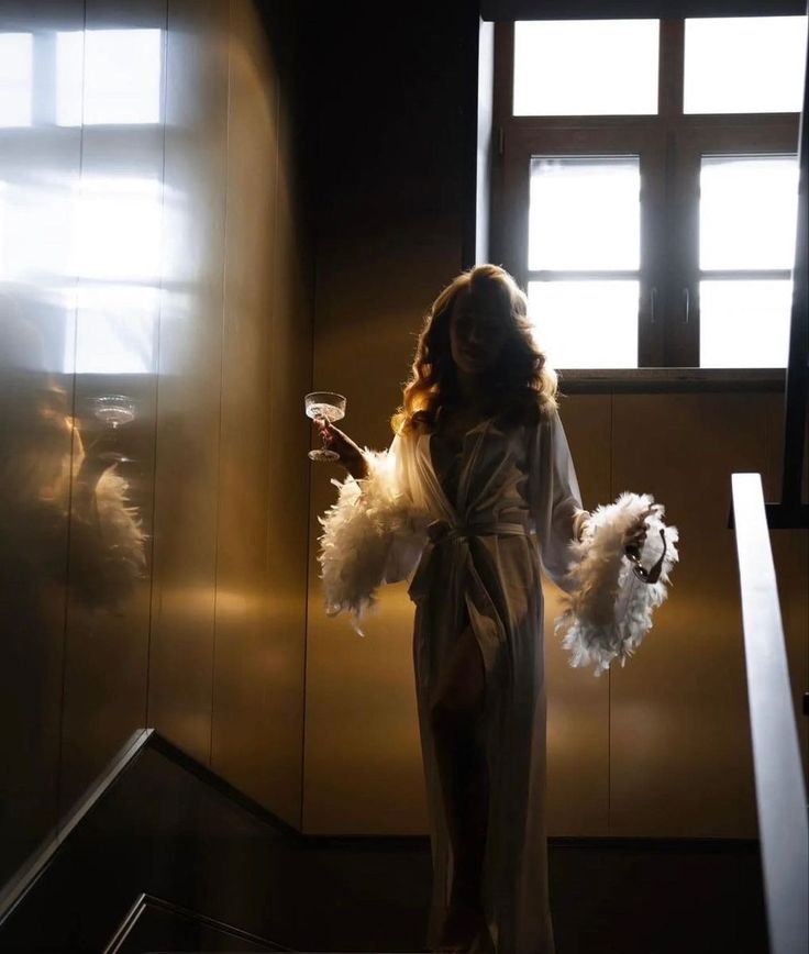 a woman in a bathrobe holding a glass of wine and standing on some stairs