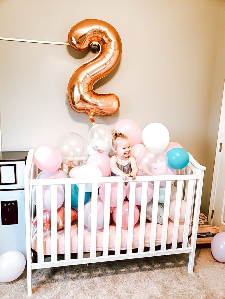 a baby in a crib with balloons and a number 2 balloon on the wall