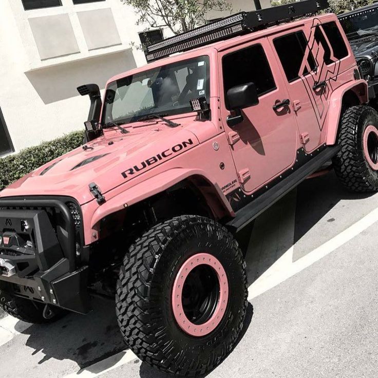 a pink jeep is parked in a parking lot next to another black car and some bushes