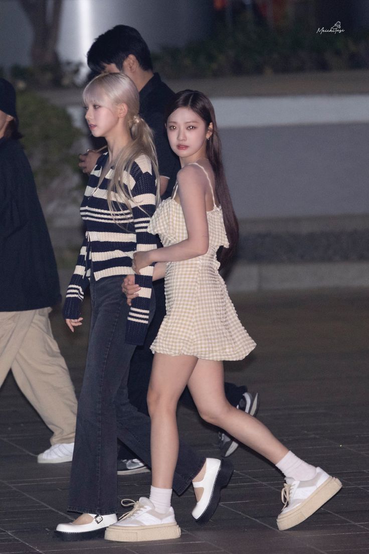 two girls are walking down the street with one girl wearing white shoes and another in black and white striped shirt