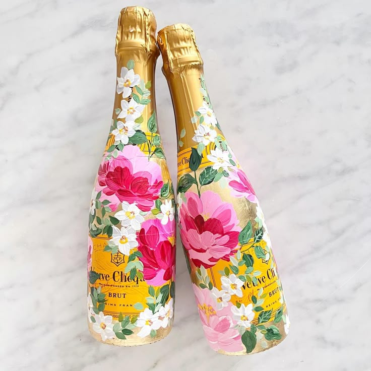 two champagne bottles with flowers on them sitting next to each other, one is gold and the other is pink