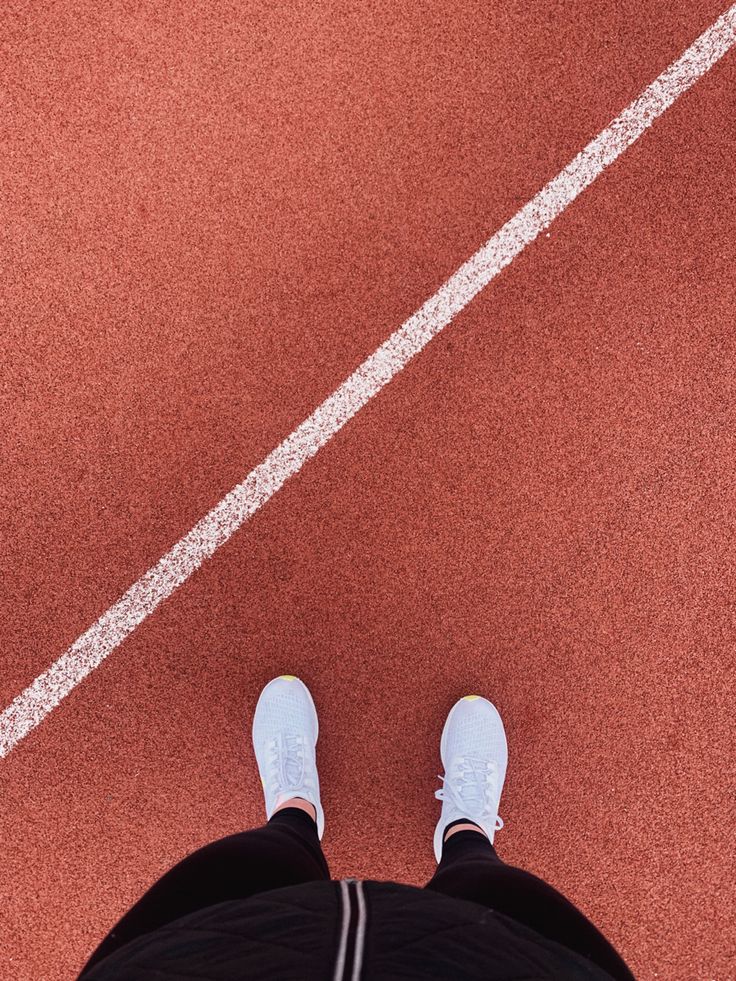 a person standing on a tennis court with their feet in the air and wearing white sneakers