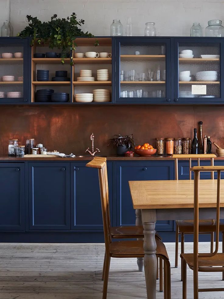 a kitchen with blue cabinets and wooden table in the foreground is a dining room