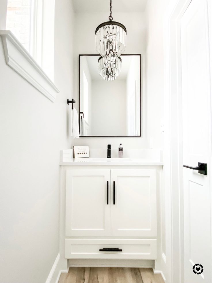 a white bathroom with a chandelier hanging from the ceiling and a mirror on the wall