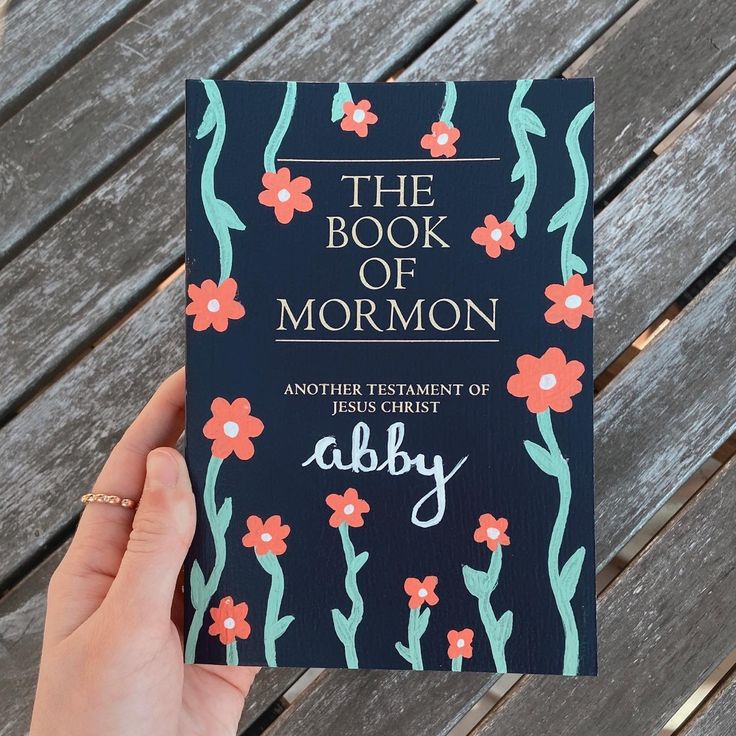 the book of mormon is being held by someone's hand on a wooden bench