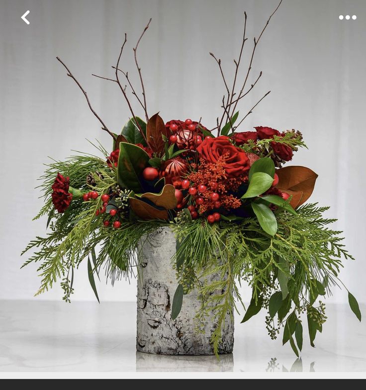 a vase filled with red flowers and greenery