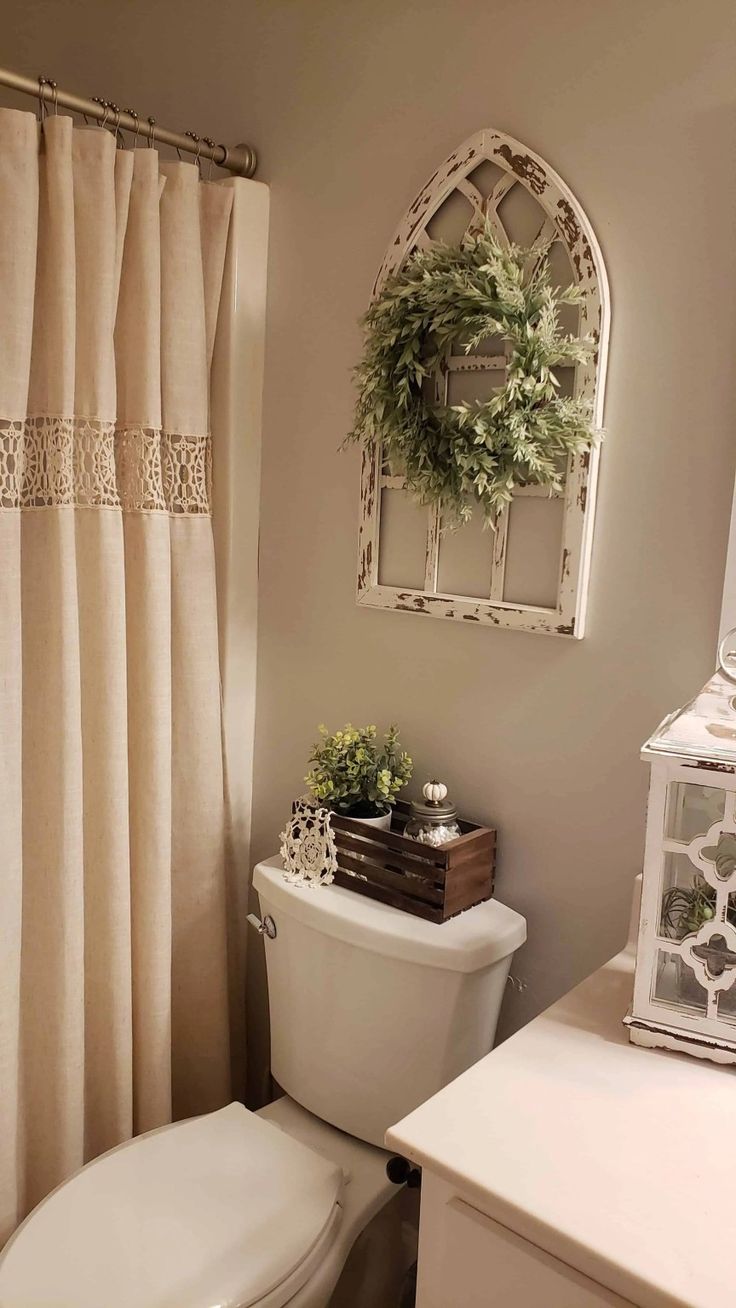 a white toilet sitting next to a shower curtain in a bathroom under a window with a wreath on top of it