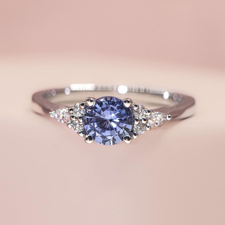 a tan and white gold ring with a blue sapphire surrounded by diamonds on a pink background