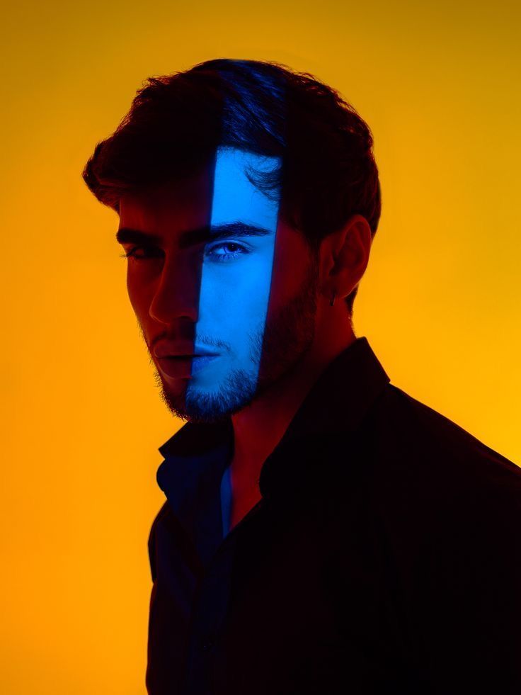 a man with blue and yellow lines painted on his face looking at the camera while standing in front of an orange background