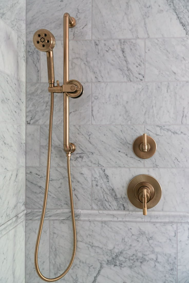 a shower head and hand shower in a white marble bathroom with gold fixtures on the wall