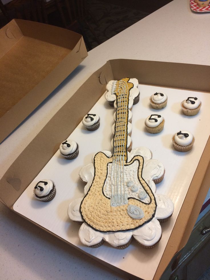 a cake shaped like a guitar and cupcakes in a box on a table