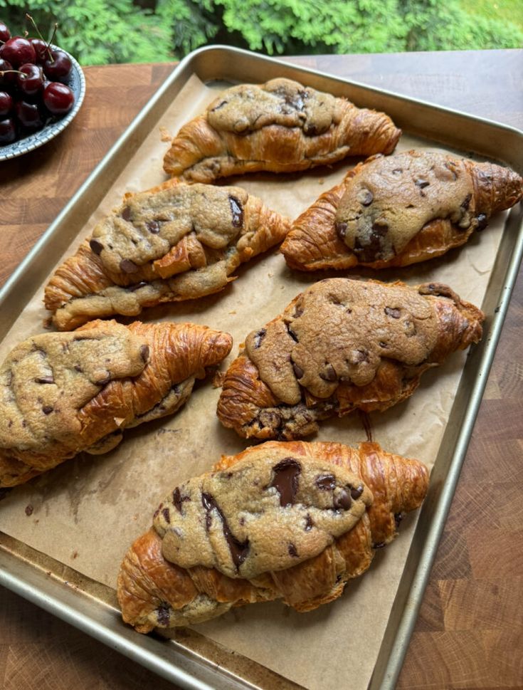 chocolate chip cookies and croissants on a baking sheet with cherries in the background