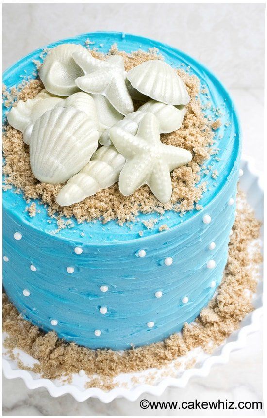 there is a blue cake decorated with sea shells and sand on the bottom, along with white polka dots