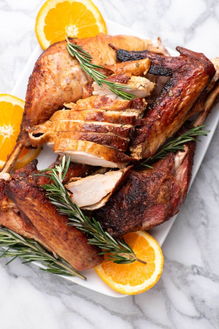 two roasted turkeys with orange slices and rosemary garnish on a white platter