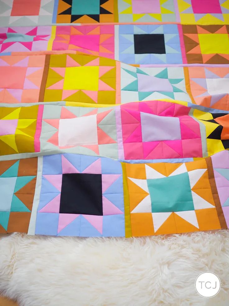 a colorful quilt is laying on top of a fluffy white furnishing next to a bed